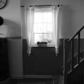 Minimalist black and white interior featuring a stove, window with curtains, and wooden stairs.