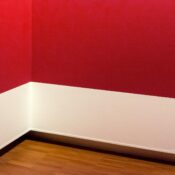 A minimalist room corner with striking red walls and wooden flooring, showcasing modern design.
