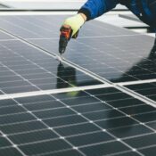 A technician uses a power tool to install solar panels, showcasing renewable energy efforts.