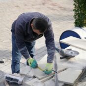 A construction worker measuring tiles outdoors with precision tools.