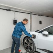 A man connects an electric car to a charging station in a modern indoor garage setting.