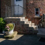 A cozy brick house entrance with stone steps and a vibrant flower pot, offering a rustic charm.