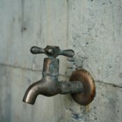 A detailed view of an aged metal faucet mounted on a textured concrete wall, revealing patina.
