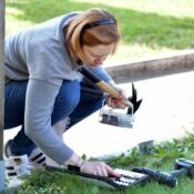 Woman kneeling with tools, engaged in DIY gardening, using a drill outdoors.