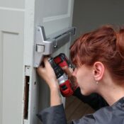 Caucasian woman focusing on door installation with power drill, side view.