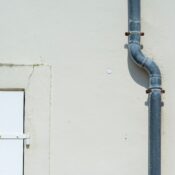 Close-up of a gray metal drainpipe attached to a plain exterior wall.