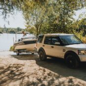 A Land Rover towing a boat to a scenic lakeside under a sunny sky.