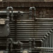 Detailed view of industrial steel pipes and a gas meter on a brick wall.