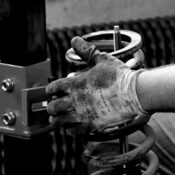 Close-up of a gloved auto mechanic's hand working with a spring in a workshop.