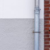 Close-up of a brick wall with a metal drainpipe against a textured white wall.