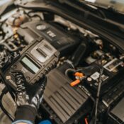 Mechanic diagnosing a car engine with a diagnostic tool, showcasing technical expertise and automotive care.