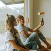 A young couple sits indoors planning their home renovation with a paint roller.