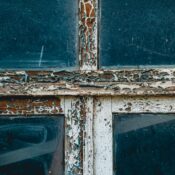 Detailed view of peeling paint on a rustic wooden window frame, showcasing texture and decay.