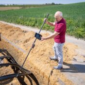 Adult male engineer using surveying equipment at a trench site on a sunny day.