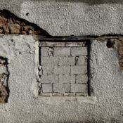 Close-up of a weathered wall with exposed brick and rough texture, showcasing rustic architecture.