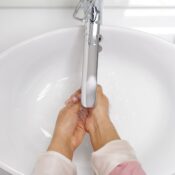 A woman washing her hands under a chrome faucet in a white sink, emphasizing hygiene.