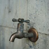 A detailed view of an aged metal faucet mounted on a textured concrete wall, revealing patina.
