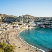 A vibrant summer scene at Matala Beach in Crete, Greece, showing sunbathers and swimmers enjoying the sun.