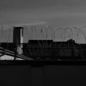 Silhouette of barbed wire fence with buildings in the background under a moody sky.