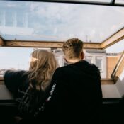 Back view of faceless couple in casual clothes hugging while standing near open window and looking at city