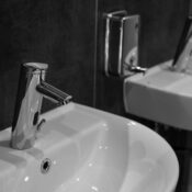 Close-up of a modern stainless steel faucet and sink in a minimalist bathroom setting.