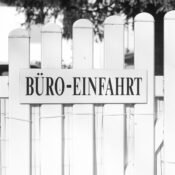 Black and white photo of an office entrance sign on a white picket fence with a tranquil setting.