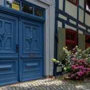 Traditional timbered house with a vibrant blue door and colorful floral decor under the summer sun.