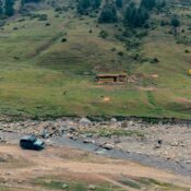 Aerial view of a serene hillside landscape with a stream, vehicle, and tents in Kashmir.