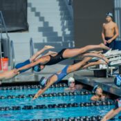 Athletes diving into a swimming pool during a competitive race at an outdoor event.