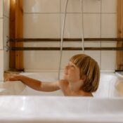 A young boy smiles in a modern, cozy bathroom characterized by warm wooden elements.