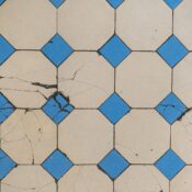 Top view of a cracked geometric tile pattern featuring blue diamond tiles on a beige background.