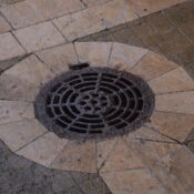 Close-up of an intricate iron manhole cover on a paved urban sidewalk.