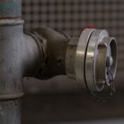 Close-up of a rusty metal pipe fitting with a cap and chain indoors in Almere.