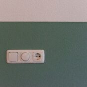 Close-up of a power outlet and switch on a textured green wall indoors.