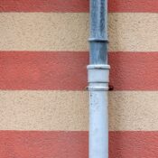 A metal drainpipe set against a red and beige striped textured wall.