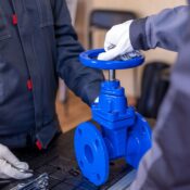 Close-up of two technicians adjusting a blue industrial valve indoors.