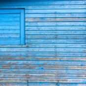 Close-up of a weathered blue wooden building wall with peeling paint and natural texture.
