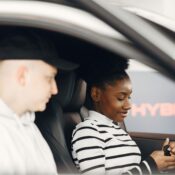 A man and woman sitting inside a hybrid car, discussing its features, highlighting modern eco-friendly transportation.
