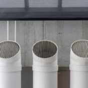 Three white industrial ventilation pipes aligned on concrete wall.