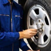 Mechanic in blue coveralls inspecting a car tire in an auto repair workshop.