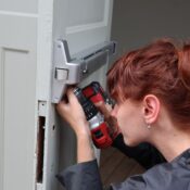 Caucasian woman focusing on door installation with power drill, side view.