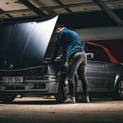 A man works on the engine of a classic convertible car in a garage, highlighting automotive repair.