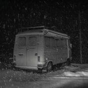 A mini van covered in snow during a snowy winter night, captured in black and white.