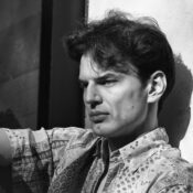 A thoughtful man in black and white, deep in contemplation against a sunlit wall.