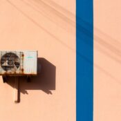 Rusty air conditioning unit casting shadow on a peach wall with blue stripe.